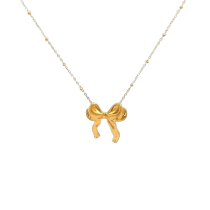 Scandal Kiss gold-plated stainless steel bow pendant necklace on a delicate beaded chain against a white background.