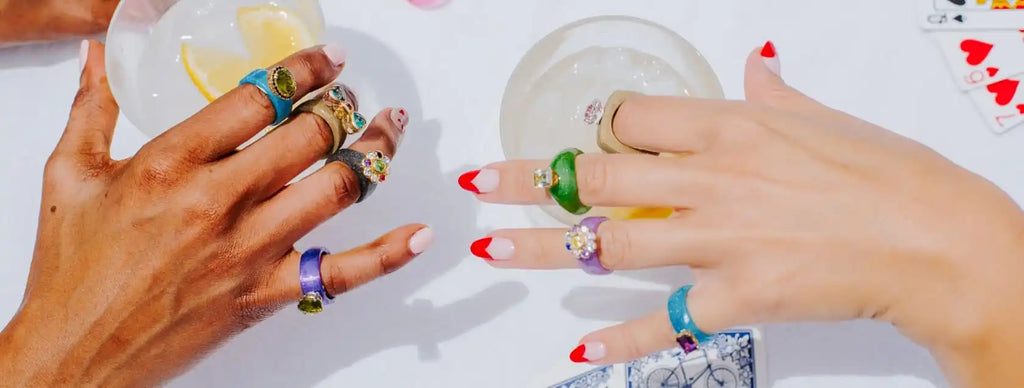 Two hands adorned with colorful rings and red-tipped manicures.