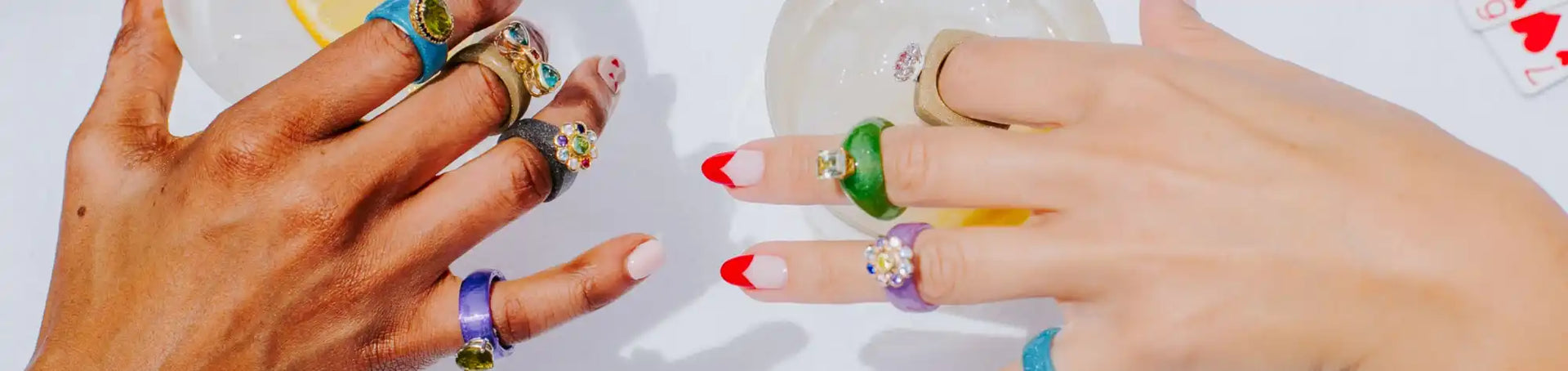 Two hands adorned with multiple colorful rings and red-tipped fingernails.